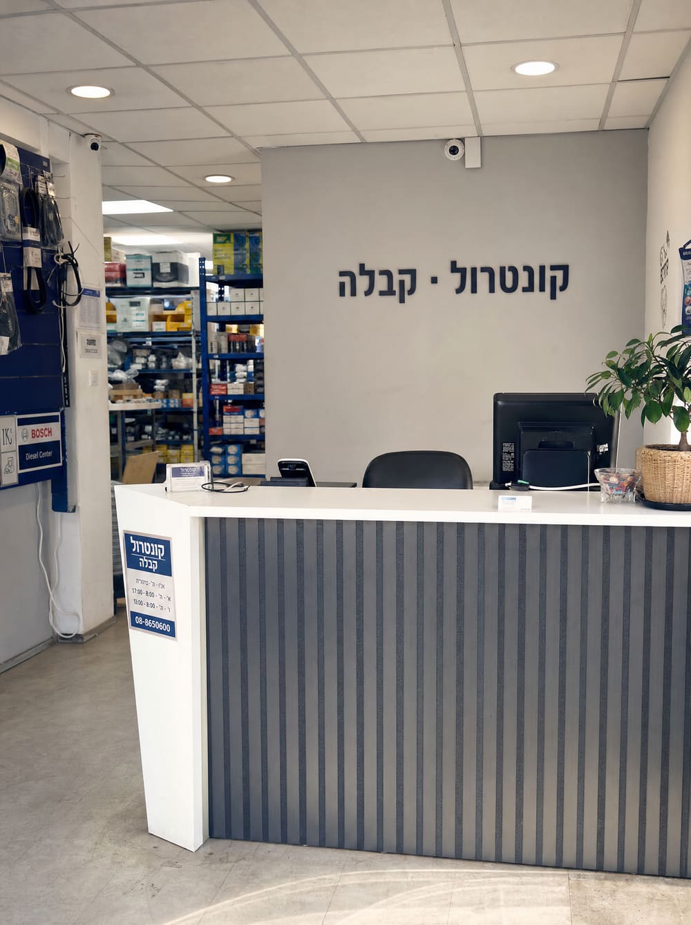 קבלת המשרד של Kontrol באשדוד — חלל קטן וחם באור יום ישראלי, מדפי חלקים מאחורי דלפק